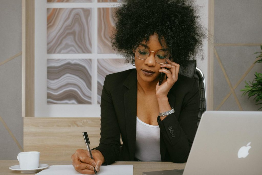 Femme d'affaires passant un appel téléphonique tout en travaillant à son bureau, concentrée et professionnelle.